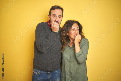 Beautiful middle age couple over isolated yellow background looking stressed and nervous with hands on mouth biting nails. Anxiety problem.