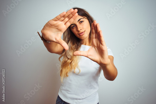 Young beautiful woman wearing casual white t-shirt over isolated background doing frame using hands palms and fingers, camera perspective