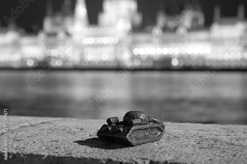 Small sculpture of tank on Danube river bank in Budapest to memorize Soviet invasion in October 1956, opposite of parliament bulding, at night, monochrome black and white