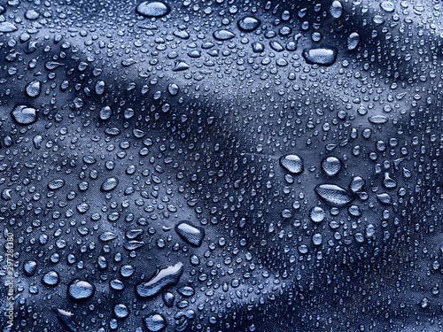 Rain water droplets on blue fiber waterproof fabric. Blue background.