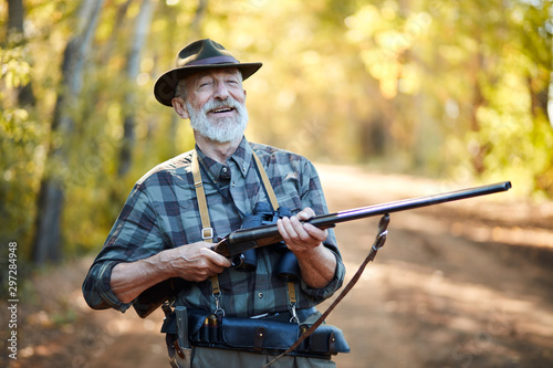 Cheerful man with holding gun with both arms, laugh. Hunting season opened, in forest