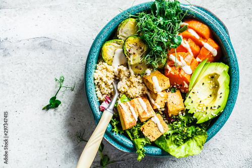 Buddha bowl with quinoa, tofu, avocado, sweet potato, brussels sprouts and tahini dressing, top view. Healthy vegan food concept.