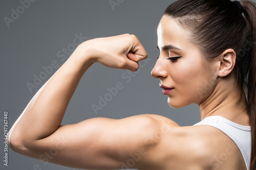 Portrait of a beautiful fitness woman showing her biceps isolated on gray background