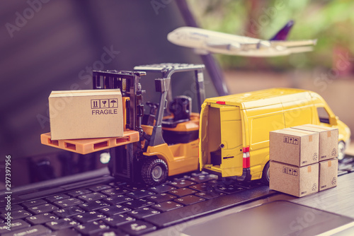 Logistics, supply chain and delivery service concept : Fork-lift truck moves a pallet with box carton. Van on a laptop computer, depicts wide spread of products around globe in ecommerce popular era