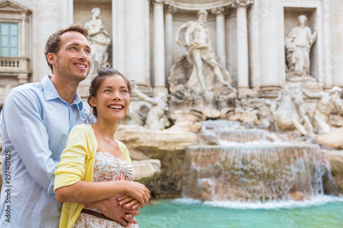 Rome travel tourists couple at Trevi Fountain in Rome, Italy vacation. Happy young romantic interracial couple traveling in Europe. Man and Asian woman embracing together.