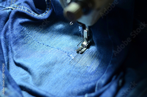 Stitching, stitching a hole in blue jeans with a sewing machine. Part of sewing machine and jeans cloth closeup. Tailoring