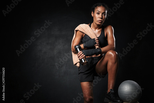 Image of african american woman holding water bottle by fitness ball