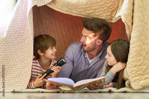 Vater und Kinder mit Taschenlampe beim vorlesen