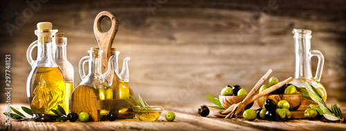 Fresh olives in rustic bowls on old wooden table. Virgin olive oil in clear glass bottles copy space. Panorama or banner concept.
