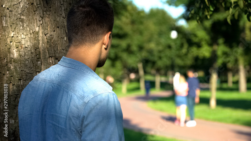 Man secretly spying loving couple walking on date outdoors, jealous ex-boyfriend