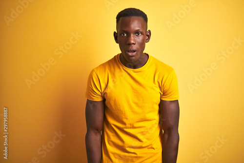 Young african american man wearing casual t-shirt standing over isolated yellow background afraid and shocked with surprise and amazed expression, fear and excited face.
