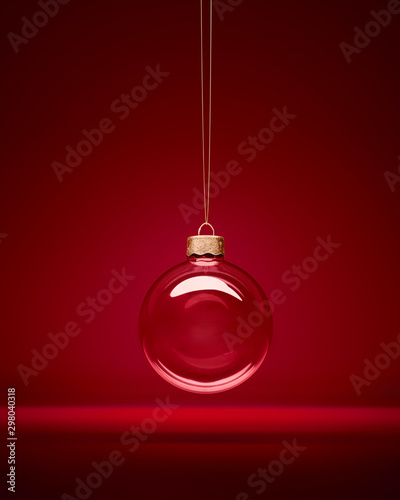 Christmas glass bauble hanging in front of luxury dark red background. Transparent winter decoration.