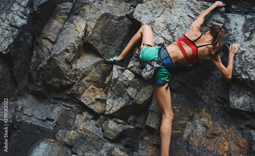Sports woman with slim fit body climbing on the rock, having workout, climber makes a hard move.