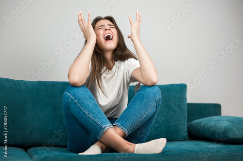 beautiful young woman crying feeling very depressed sitting on the sofa with her arms up