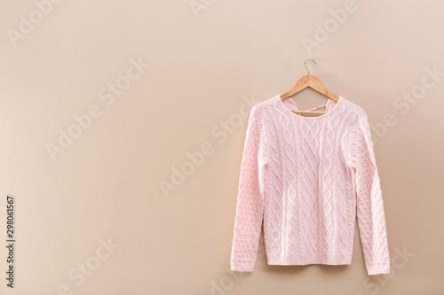 Hanger with stylish sweater on beige wall. Space for text