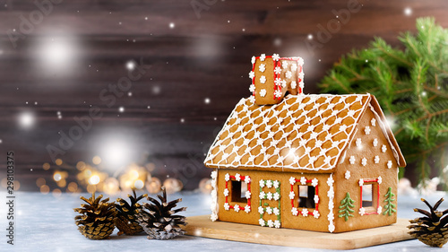 Sweet decorated gingerbread house closeup with pine cones decorations, fir tree branches, bokeh and snowfall. Christmas card with dark background, copy space