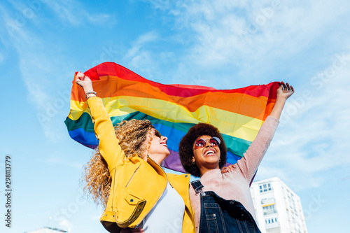 Two women friends hanging out in the city waving LGBT with pride flag