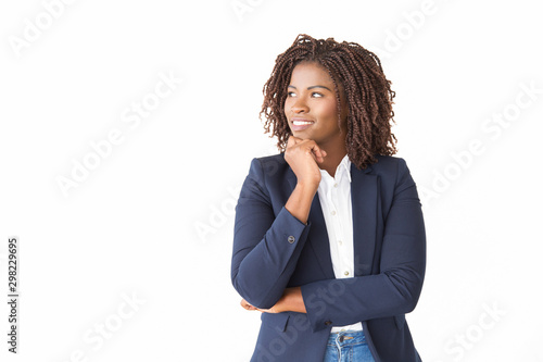 Happy pensive female agent looking at copy space away. Young African American business woman standing isolated over white background, leaning chin on hand, smiling. Advertising concept