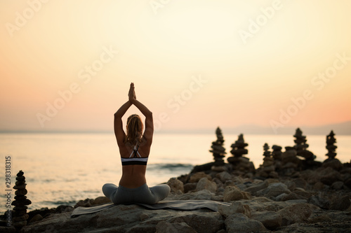 Back view of woman meditating on the beach at sunset.
