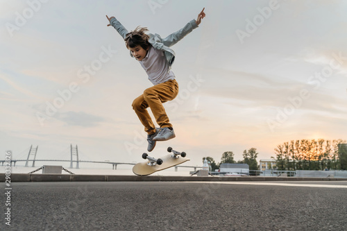 Boy jumping on skateboard at the street. Funny kid skater practicing ollie on skateboard at sunset.
