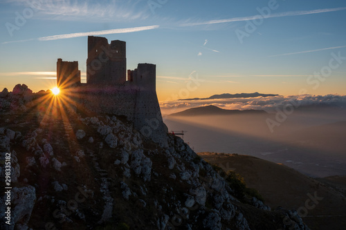 Ruins of medieval castle of Rocca Calascio at sunny morning, with foggy landscape in background and sunstar, Abruzzo, Italy