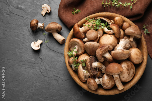 Different fresh wild mushrooms in bowl on black background, flat lay