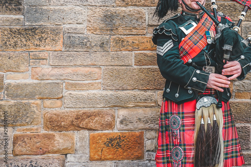 EDINBURGH, SCOTLAND, 24 March 2018 , Scottish bagpiper dressed in traditional red and black tartan dress stand before stone wall. Edinburgh, the most popular tourist city destination in Scotland..