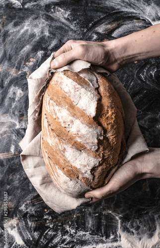 Trzymanie bochenka chleba w dłoniach na czarnym tle w stylu rustykalnym