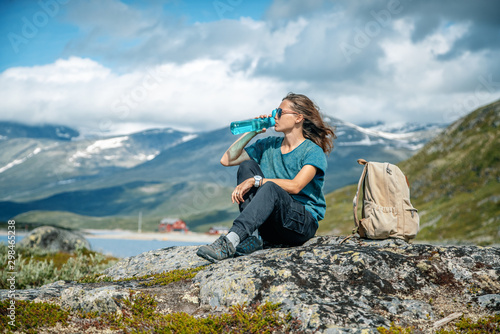Young beautiful girl traveler drinking water at a halt. Travel to Norway, beautiful mountain landscape, Jutunheimen park