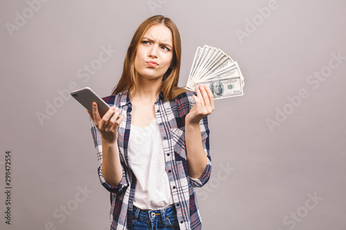 Image of excited young lady isolated over grey background. Amazed with mobile phone, holding money.