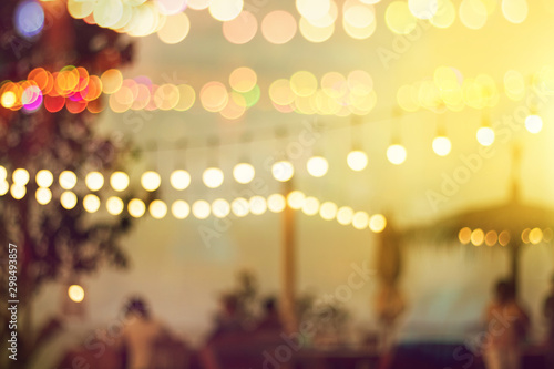 blurred bokeh light on sunset with yellow string lights decor in beach restaurant