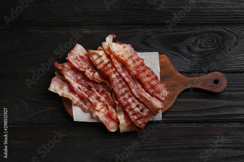 Slices of tasty fried bacon on black wooden table, top view