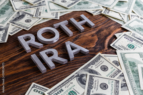 words ROTH IRA laid on wooden surface by metal letters with us dollar banknotes