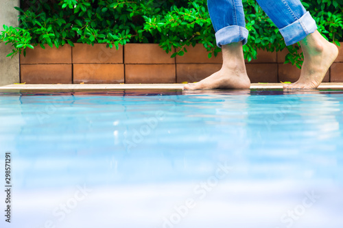 Young man wearing blue Jean walking alone at the edge of the swimming pool ,Bricks and tree leaves are the background.