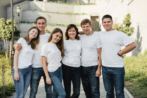 Happy family in white T-shirt and jeans emracing and having fun. Parents with their adult children walking in the park. Family time concept
