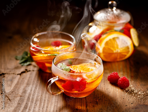Fruit hot tea with the addition of oranges, lemons, mandarins and raspberries in a glass cups on a wooden table. Healthy hot drink