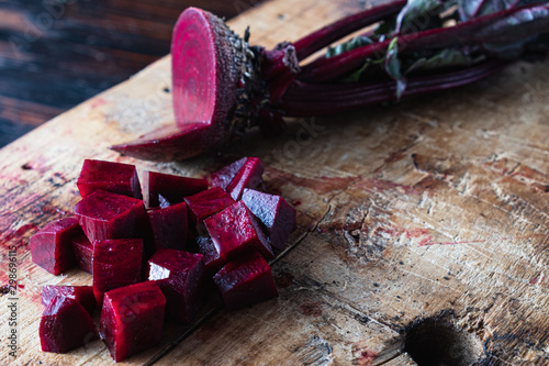 one juicy beets with leaves, one of which sliced lies next to diced beets on a wooden board
