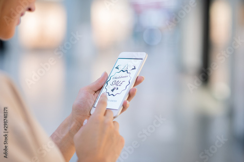 Hands of young woman holding smartphone and scrolling through online shop