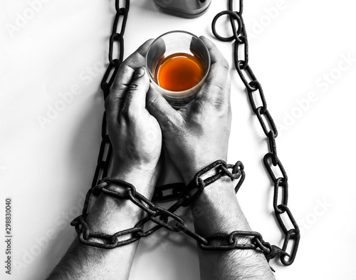 Man's hands in old rusty chains near the bottle. Addicted to alcohol. Dangerous habit.