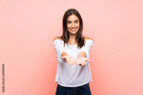 Young woman over isolated pink background holding copyspace imaginary on the palm to insert an ad