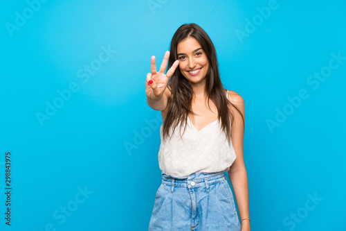 Young woman over isolated blue background happy and counting three with fingers