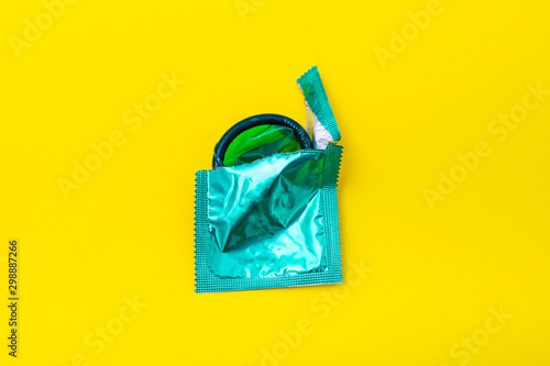 Condom half out of package on a yellow background. A condom use to reduce the probability of pregnancy or sexually transmitted disease (STD). Safe sex and reproductive health concept.