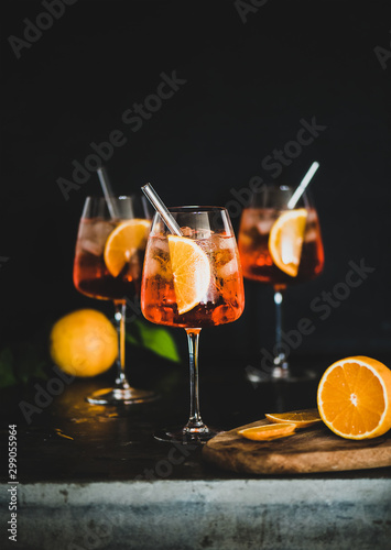 Aperol Spritz aperitif with oranges and ice in glass with eco-friendly glass straw on concrete table, black background, selective focus, copy space. Summer refreshing drink concept