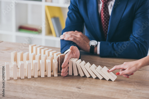 cropped view of woman pushing wooden block and risk manager stopping domino effect