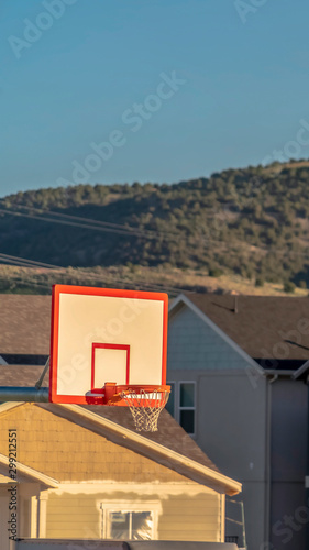 Vertical Focus on a basketball ring and board against houses on a sunny day