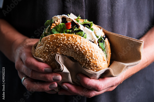 Woman is holding a bagel fresh burger before eating. Top view shot. Gourmet conception.