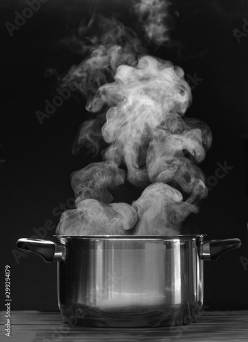 Steaming pot on black background. Smoke above boiling soup pot. 