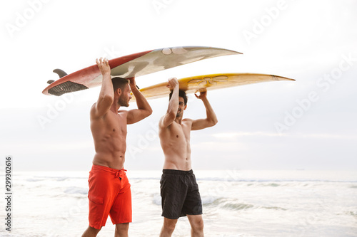Two men surfers friends with surfings on a beach outside.