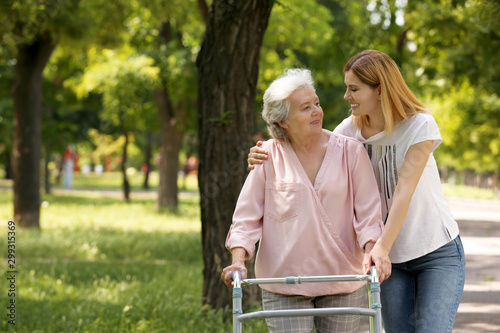 Caretaker helping elderly woman with walking frame outdoors