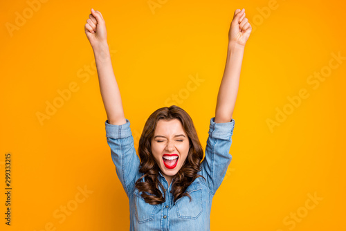 Photo of overjoyed rejoice girl shutting her eyes in a fit of happiness raising her hands celebrating her victory isolated over yellow vivid color background